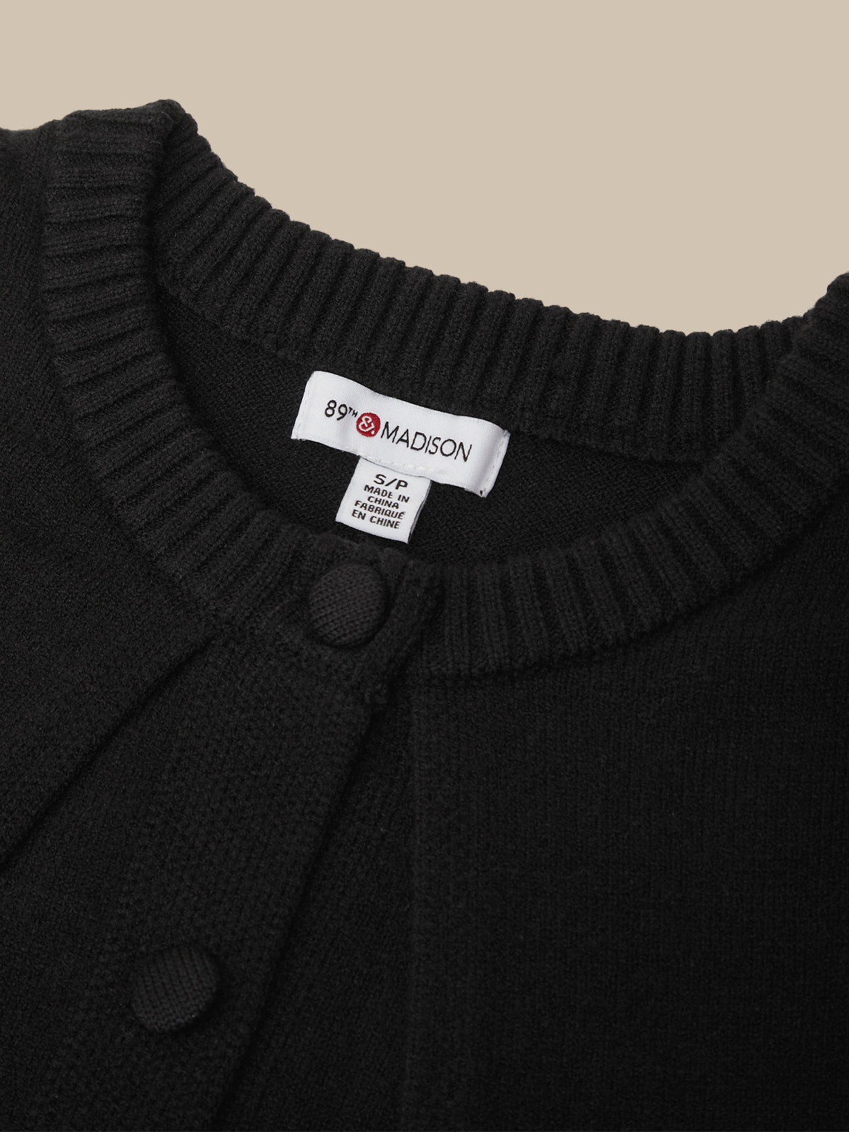 Close-up of a black ribbed-knit cardigan sweater with a white neck label reading 89 Madison.