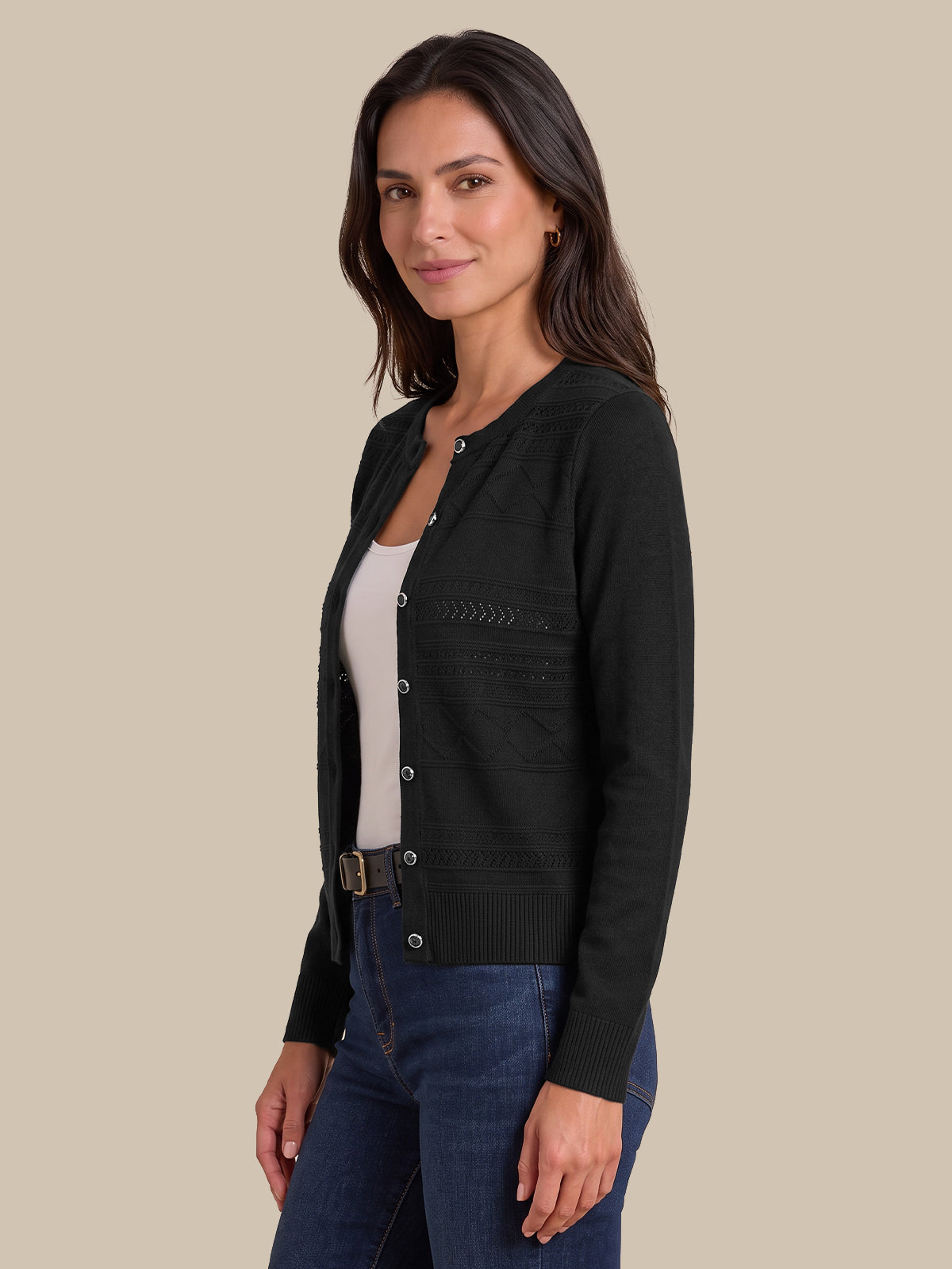 A woman modeling a black long-sleeve knit cardigan with decorative textured patterns on the chest, worn over a white top and blue jeans, set against a solid beige background.