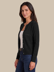 A woman modeling a black long-sleeve knit cardigan with decorative textured patterns on the chest, worn over a white top and blue jeans, set against a solid beige background.