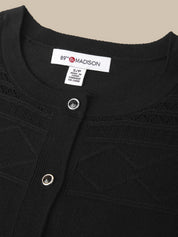 Close-up of a black knit cardigan sweater with a buttoned neckline and a visible neck label reading 89th Madison.