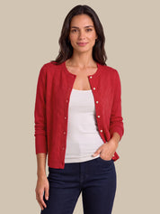 A woman modeling a red button-front cardigan over a white tank top and dark navy jeans, standing against a plain beige studio background.