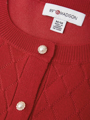 Close-up of a red knit cardigan sweater showing the ribbed collar, textured knit pattern, and two pearl-like buttons. The inner neck label reads 89th & Madison.