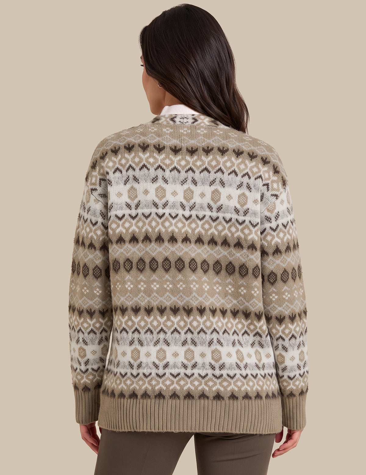 A woman viewed from the back wearing a beige and white Fair Isle patterned knit sweater, paired with brown pants, against a solid beige background.