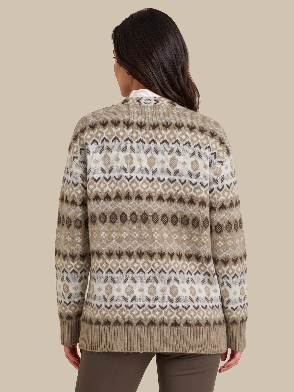 A woman viewed from the back wearing a beige and white Fair Isle patterned knit sweater, paired with brown pants, against a solid beige background.