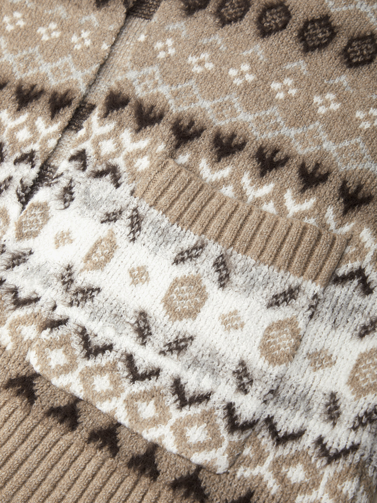 Close-up of a knitted cardigan featuring a Fair Isle pattern in beige, white, and dark brown, with ribbed knit trim.