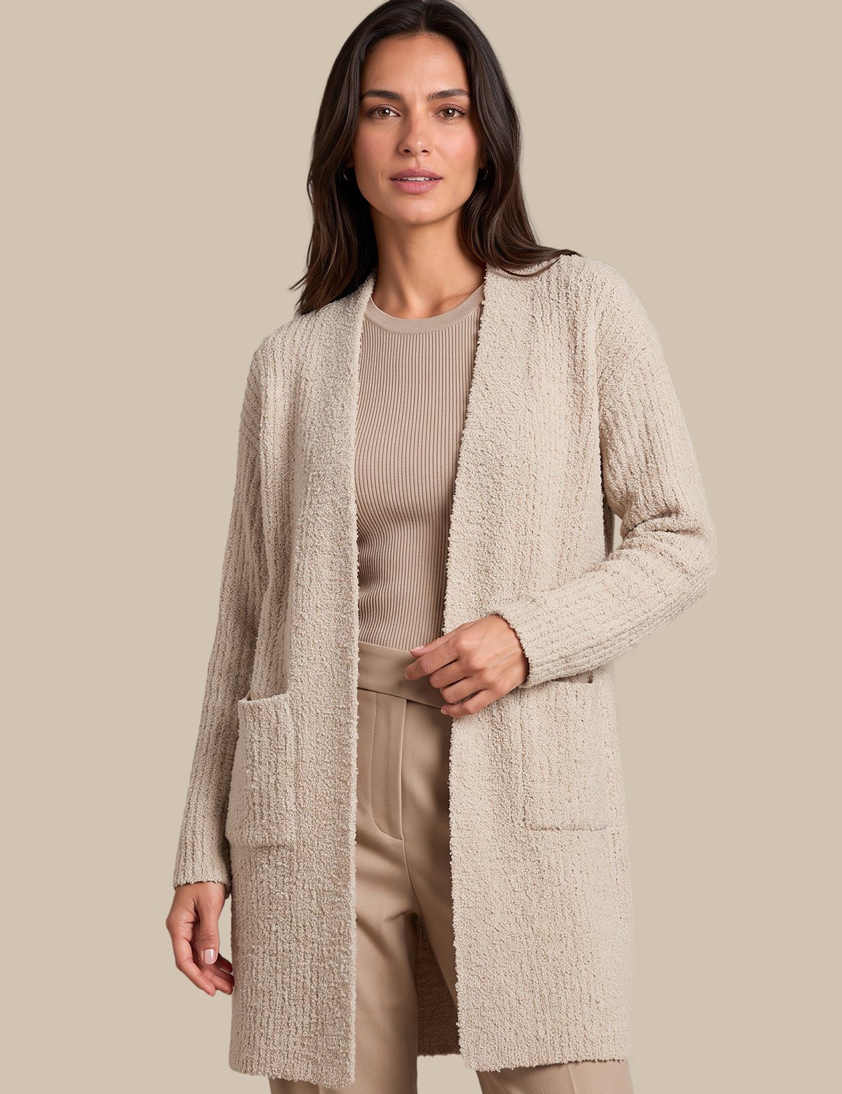 A woman modeling a textured, open-front cardigan in a light beige color, paired with a matching ribbed top and beige trousers, set against a solid beige background.