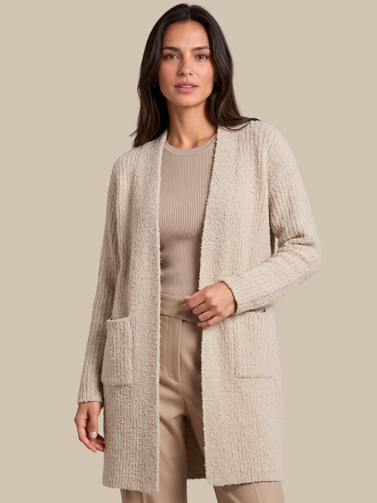 A woman modeling a textured, open-front cardigan in a light beige color, paired with a matching ribbed top and beige trousers, set against a solid beige background.