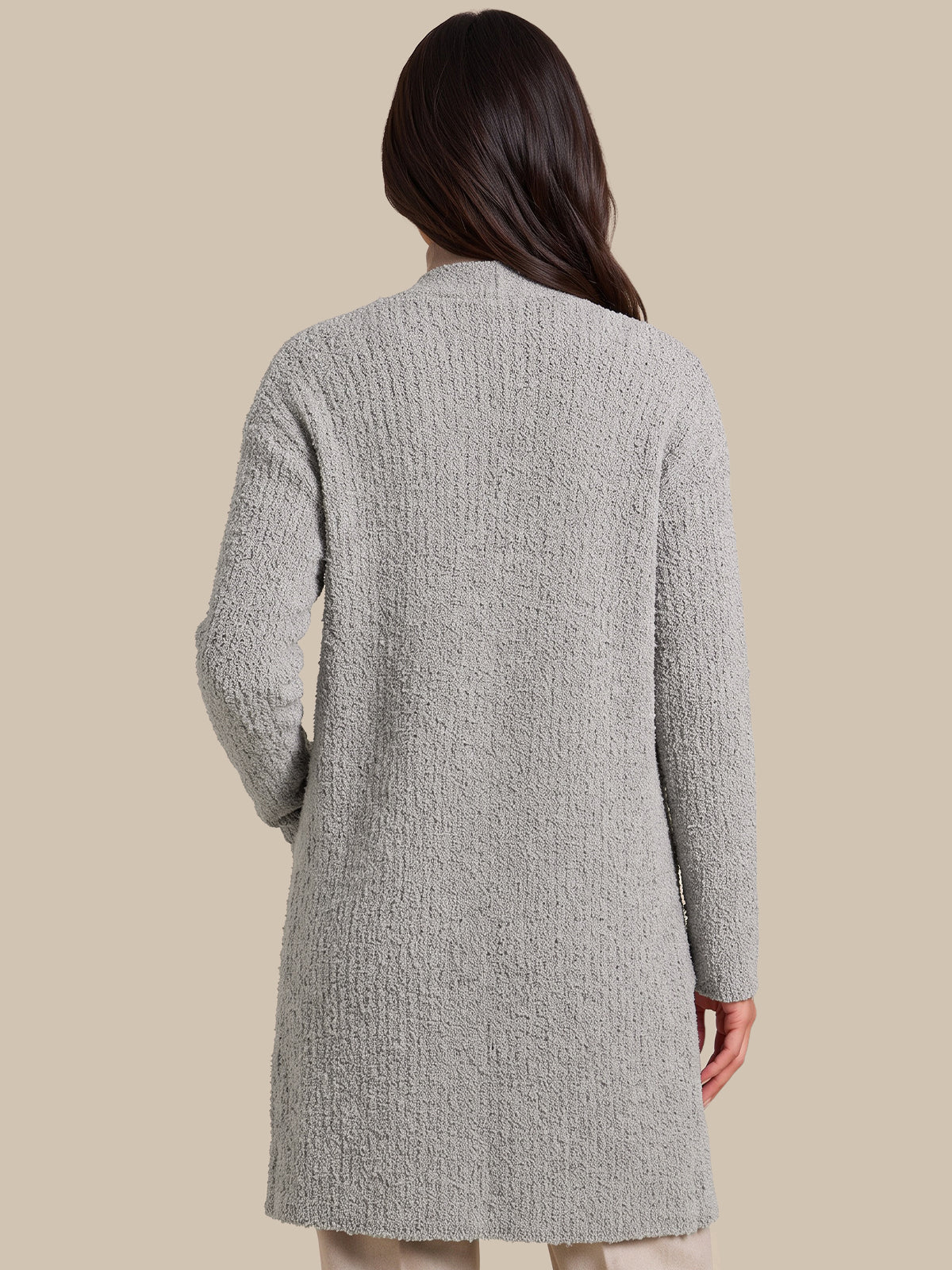 A woman shown from the back wearing a light gray textured knit cardigan sweater, set against a solid beige studio background.