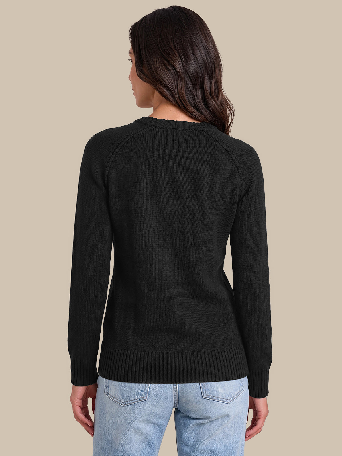 A woman shown from the back wearing a black long-sleeve knit sweater and light blue jeans, standing against a solid beige studio background.