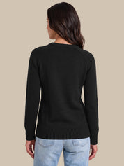 A woman shown from the back wearing a black long-sleeve knit sweater and light blue jeans, standing against a solid beige studio background.