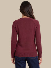 A woman viewed from the back wearing a long-sleeve ribbed knit sweater in a deep burgundy color, paired with dark blue jeans, against a solid beige background.