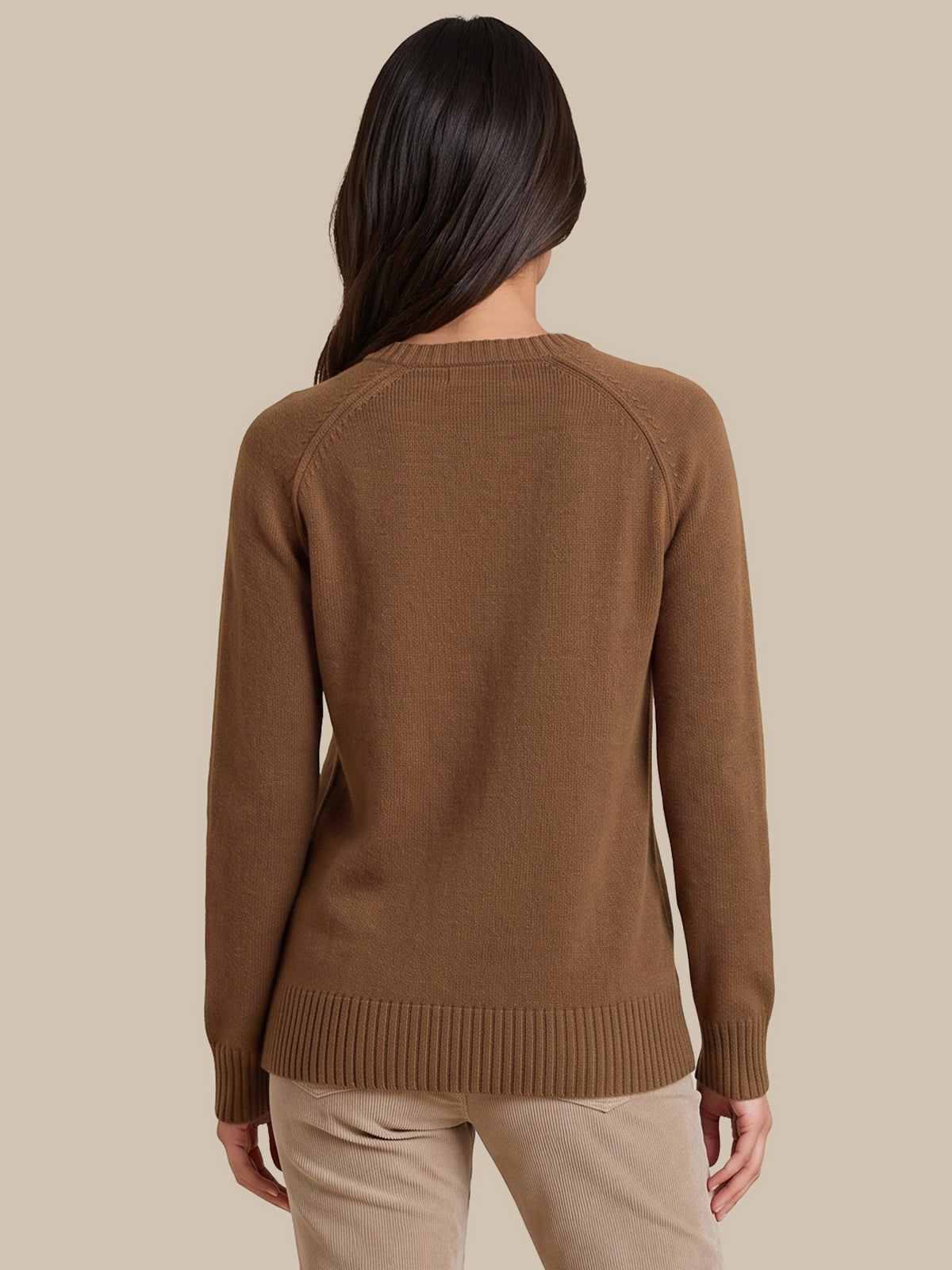 A woman viewed from the back wearing a brown ribbed knit sweater and beige pants, set against a solid beige studio background.