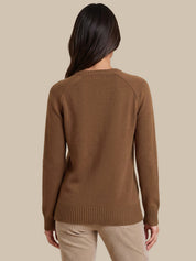 A woman viewed from the back wearing a brown ribbed knit sweater and beige pants, set against a solid beige studio background.