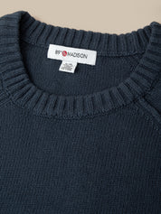 Close-up of a dark navy blue knit sweater with a ribbed crew neck, featuring a white neck label with the brand name '89° MADISON'.