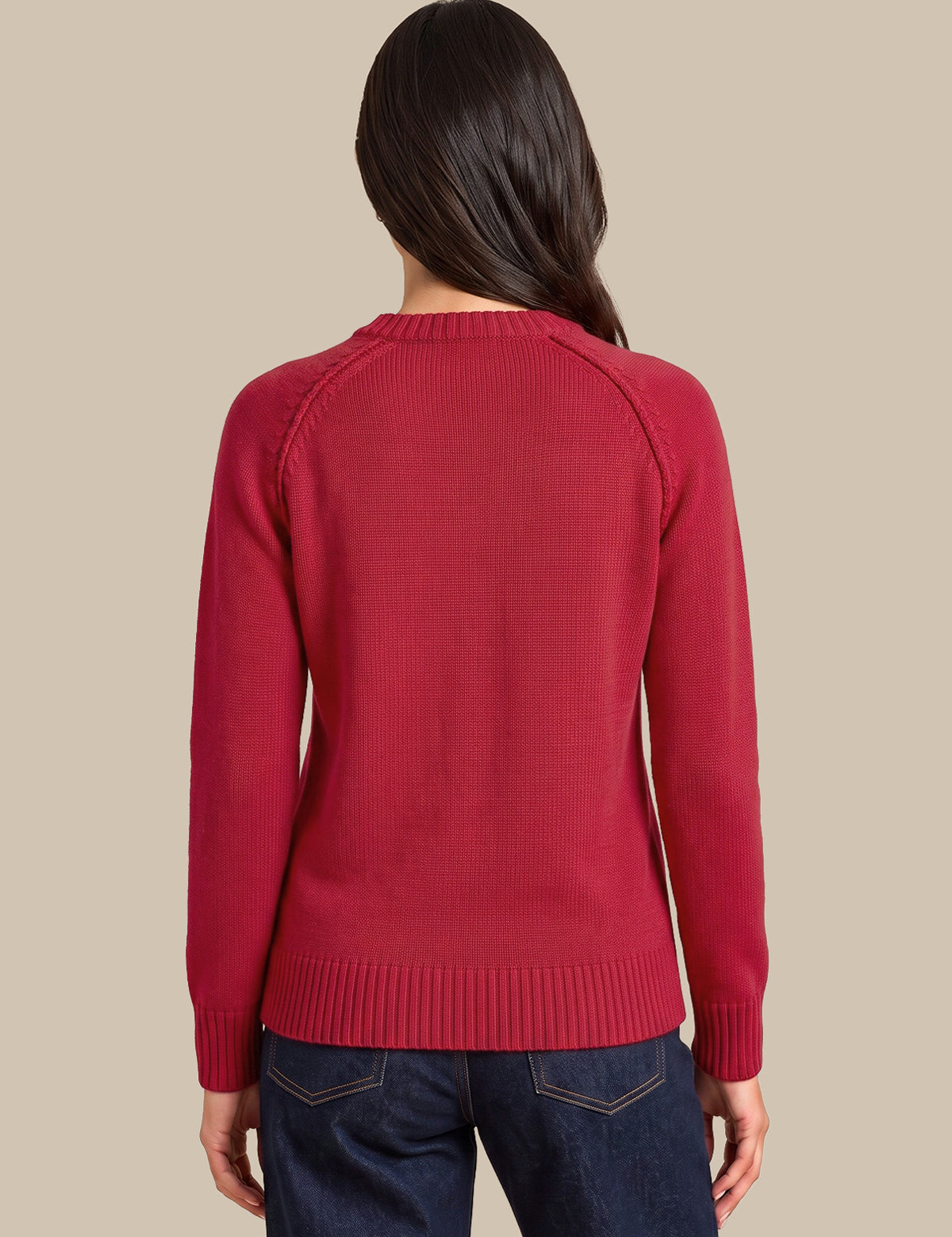 A woman viewed from the back wearing a red knit sweater and dark blue jeans against a solid beige background.