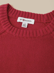 Close-up of a ribbed knit sweater in a deep berry red, showing the white neck label with the brand name 89th & Madison.