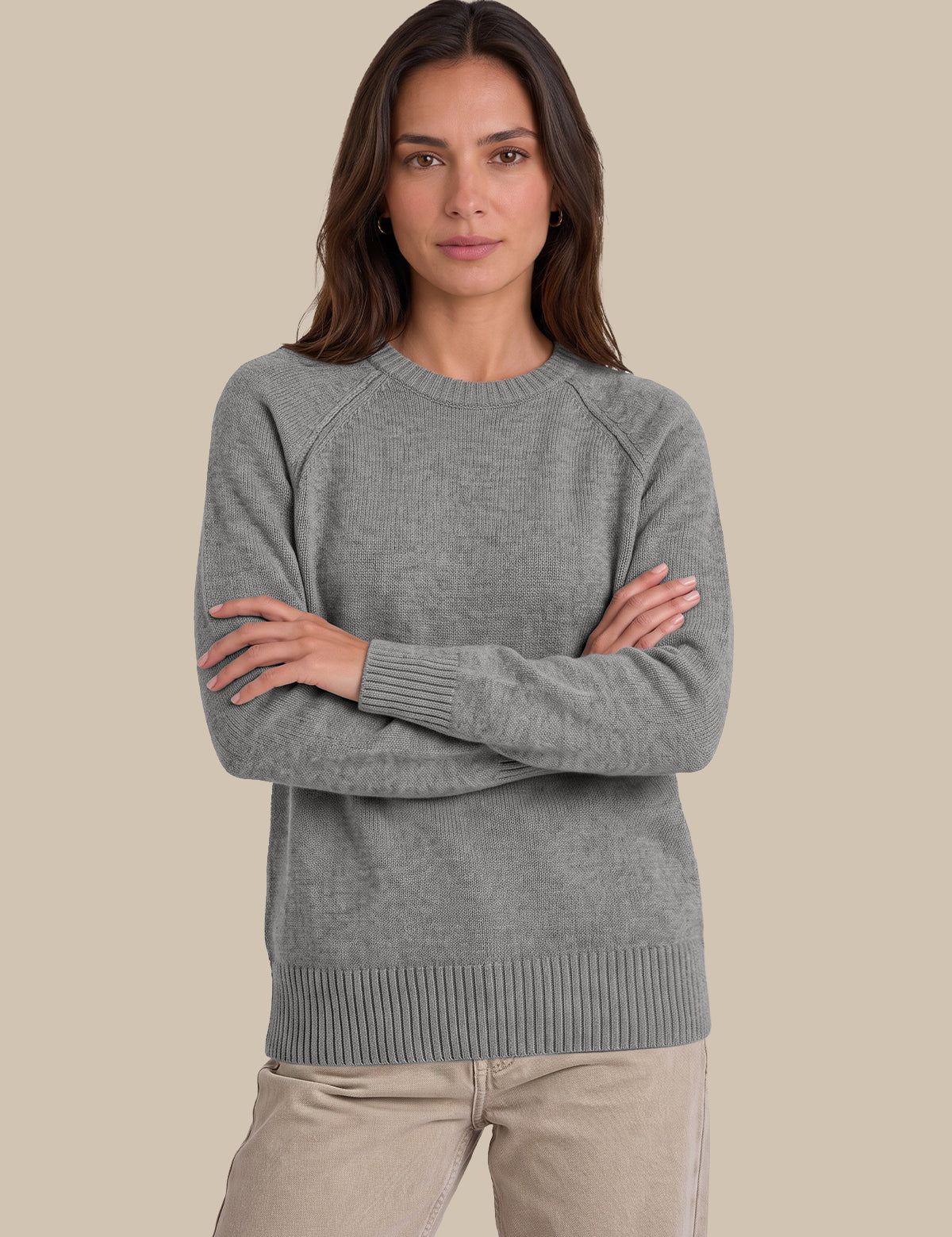 A woman wearing a heather gray crewneck sweater with raglan sleeves and ribbed cuffs, hem, and collar, paired with beige pants, set against a solid beige background.