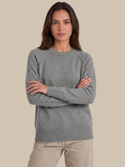 A woman wearing a heather gray crewneck sweater with raglan sleeves and ribbed cuffs, hem, and collar, paired with beige pants, set against a solid beige background.