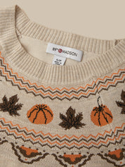 Close-up of a cream knit sweater with a pattern of orange pumpkins and dark brown maple leaves, featuring a white neck label that reads 89th & MADISON.