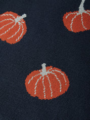 Close-up of a knit fabric featuring a repeating pattern of orange pumpkins with white stems and ribs on a dark navy blue background.