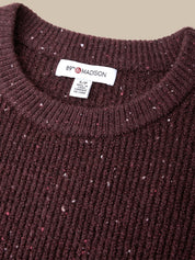 Close-up of a ribbed knit crewneck sweater in dark burgundy with small white and pink flecks, showing a white neck label that reads 89th & MADISON.