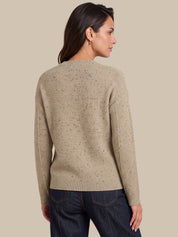 A woman shown from the back wearing a beige textured knit sweater with subtle dark speckles and dark blue jeans, set against a solid beige background.