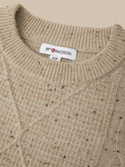 Close-up of a beige knit sweater with subtle brown and black flecks, featuring a white neck label that reads '89° MADISON'.