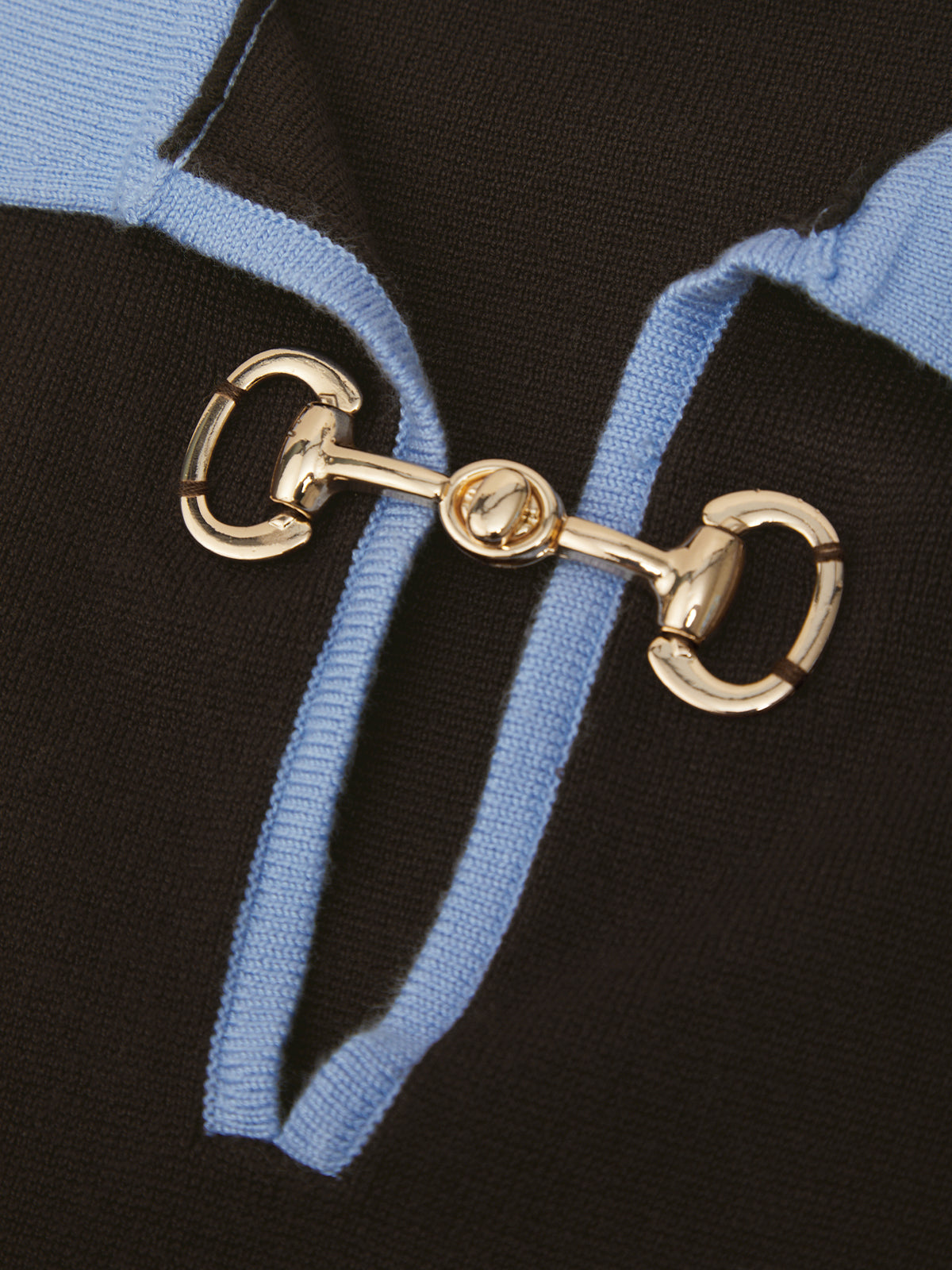 Close-up of a black knit garment featuring a light blue ribbed trim and a prominent gold horsebit hardware detail.