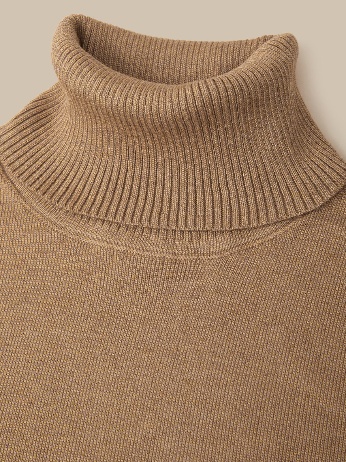 Close-up of a ribbed knit turtleneck sweater in a warm camel brown color, showing the detailed knit texture and collar.
