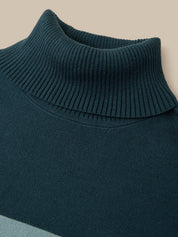 Close-up of a ribbed knit turtleneck sweater in a deep teal blue-green color, showing the texture of the collar and upper chest against a warm beige background.