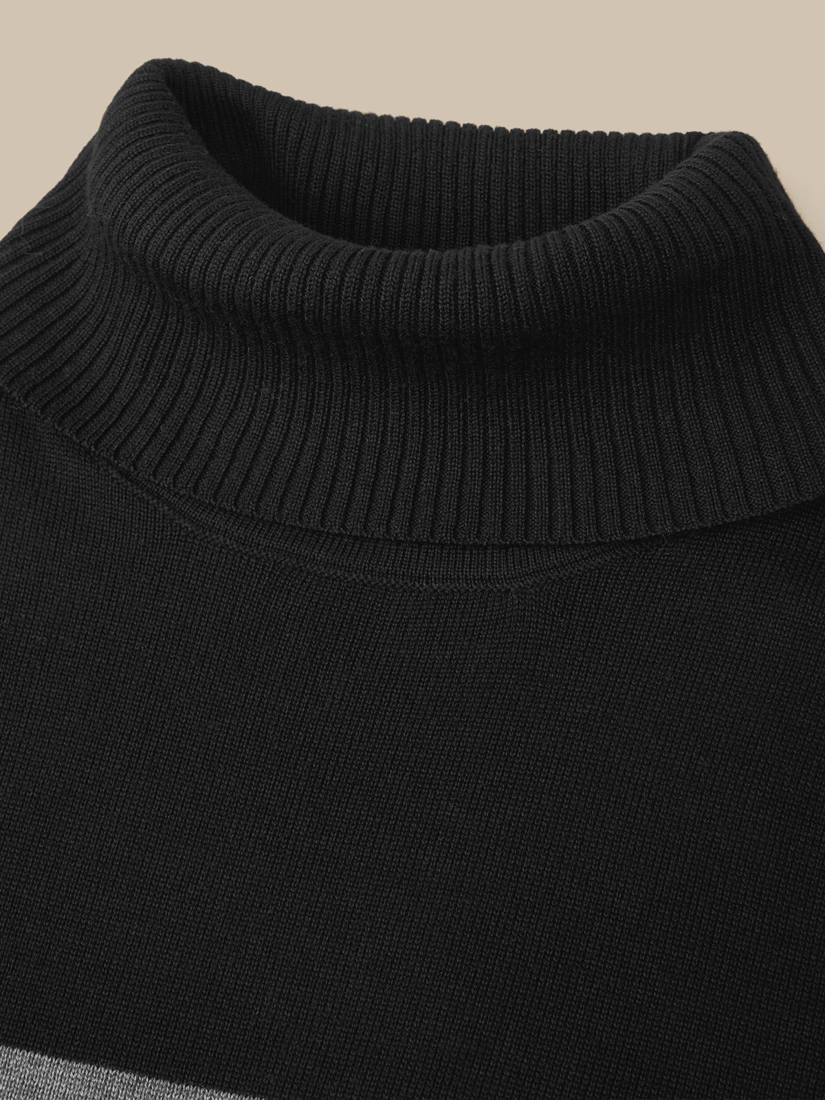 Close-up of a black ribbed knit turtleneck sweater against a solid beige background.