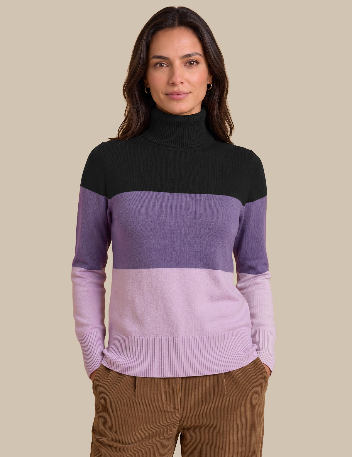 A woman wearing a color-blocked knit turtleneck sweater with a black upper section, a wide medium purple band, and a lighter lavender lower section, paired with brown corduroy pants against a solid beige background.