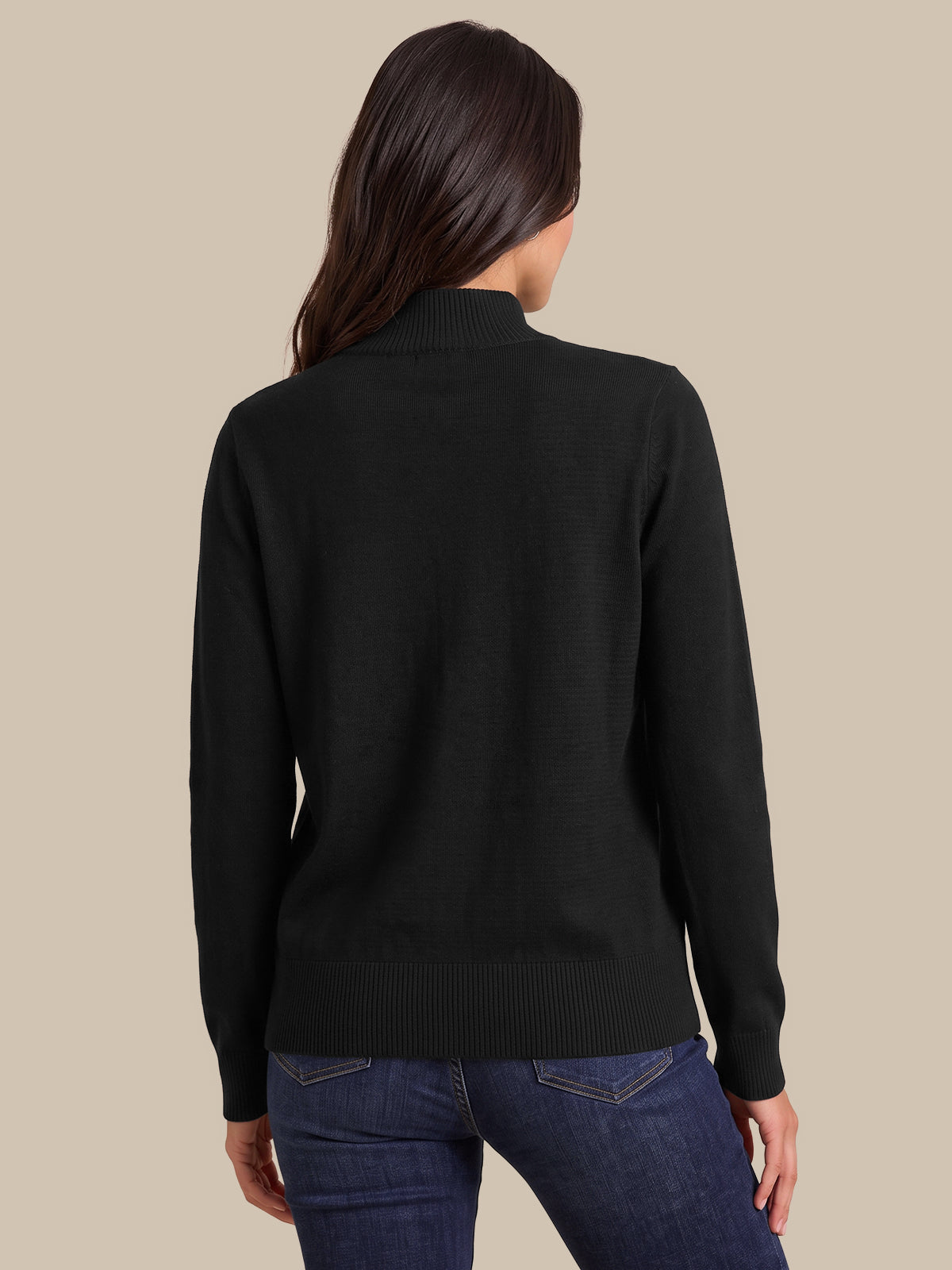 A woman shown from the back wearing a black mock neck knit sweater and blue jeans against a solid beige background.
