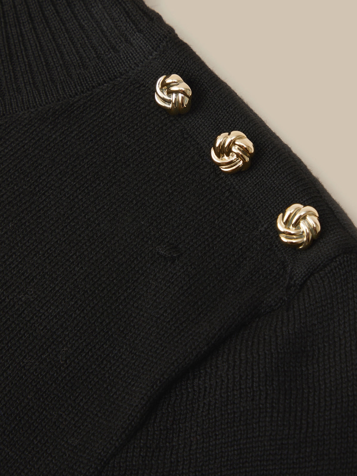 Close-up of a black ribbed knit sweater with three decorative gold-tone knotted buttons on the shoulder.