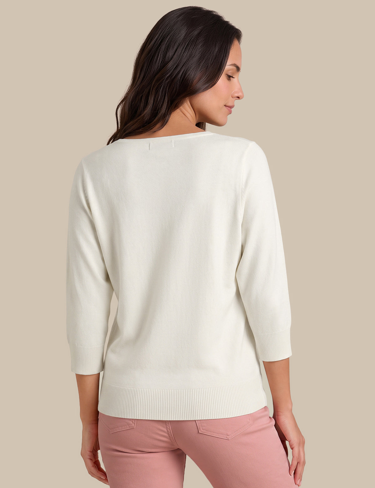 A woman shown from the back wearing a cream-colored knit sweater with three-quarter sleeves and light pink pants, set against a solid beige background.