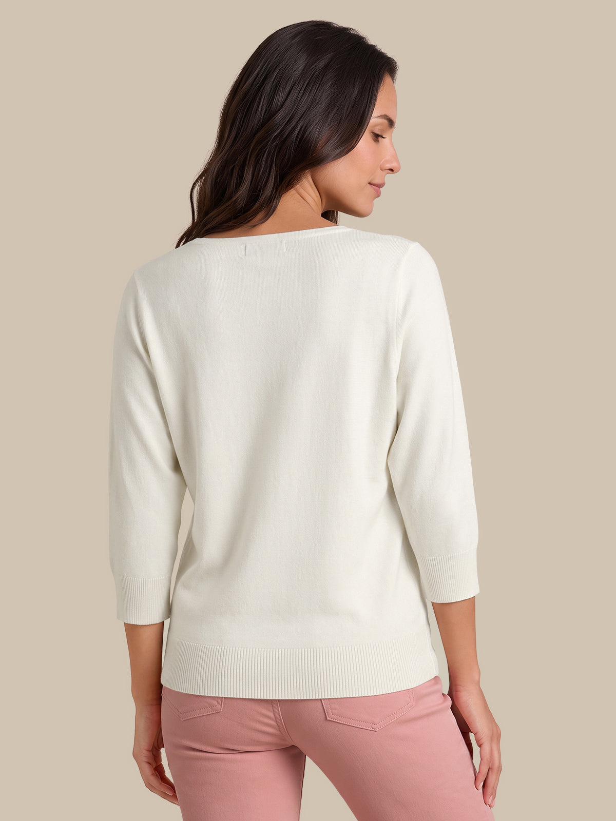 A woman shown from the back wearing a cream-colored knit sweater with three-quarter sleeves and light pink pants, set against a solid beige background.