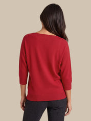 A woman shown from the back wearing a red knit sweater with three-quarter sleeves and dark gray pants, set against a solid beige background.