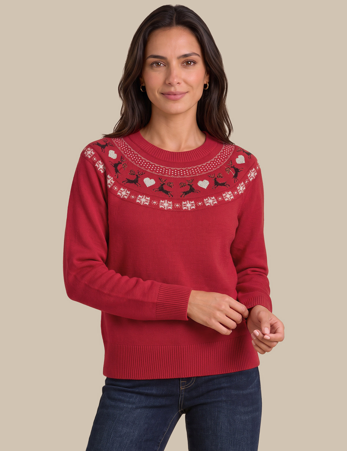 A woman wearing a red crewneck sweater with a decorative yoke pattern of white and black fair isle motifs, paired with dark blue jeans, against a solid beige background.