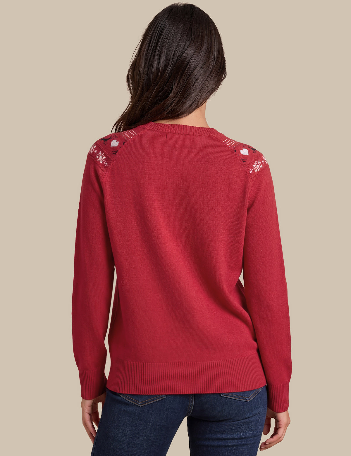 A woman viewed from the back wearing a red knit sweater with white embroidered details on the shoulders and dark blue jeans, set against a solid beige background.