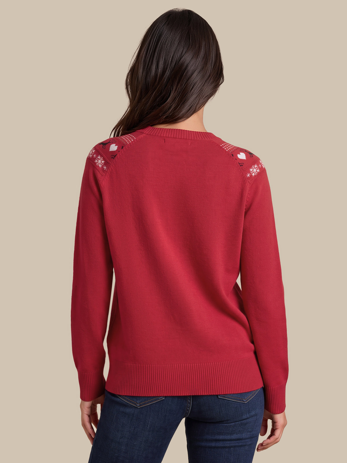 A woman viewed from the back wearing a red knit sweater with white embroidered details on the shoulders and dark blue jeans, set against a solid beige background.