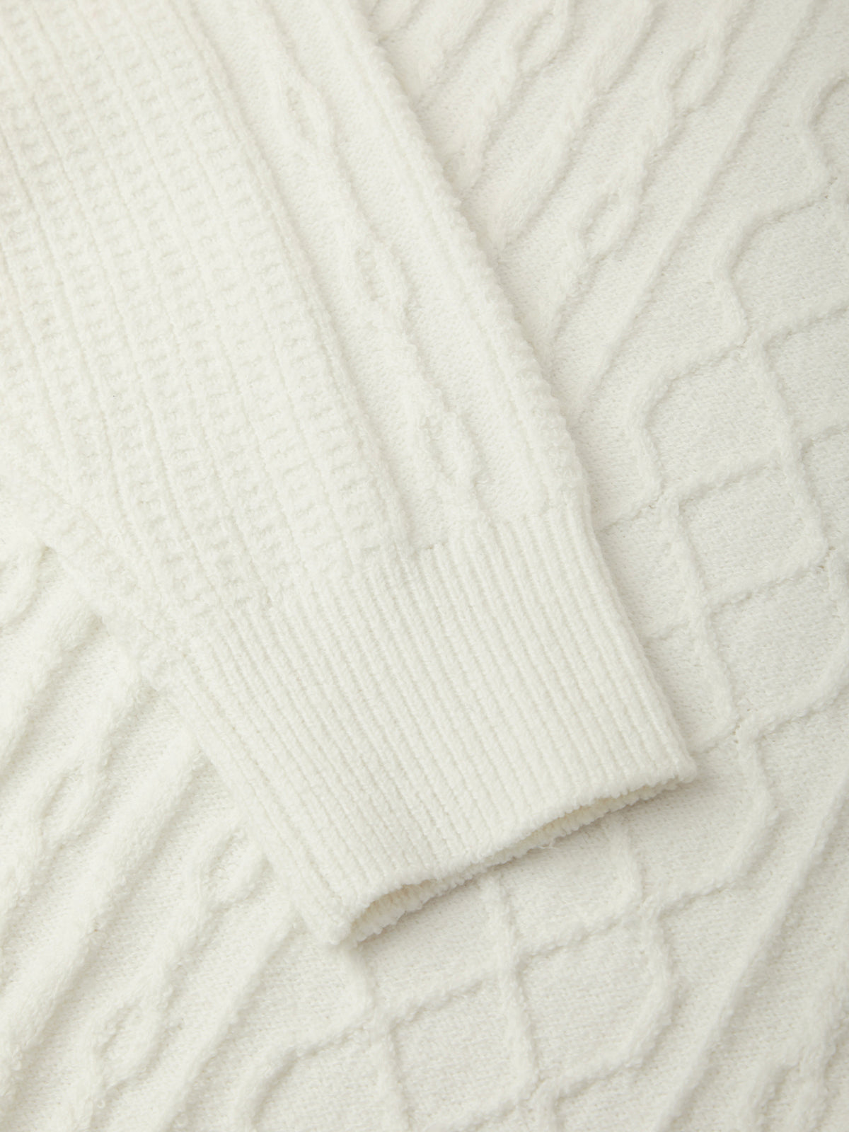 Close-up of a cream-colored cable-knit sweater showing the ribbed cuff and textured knit pattern.