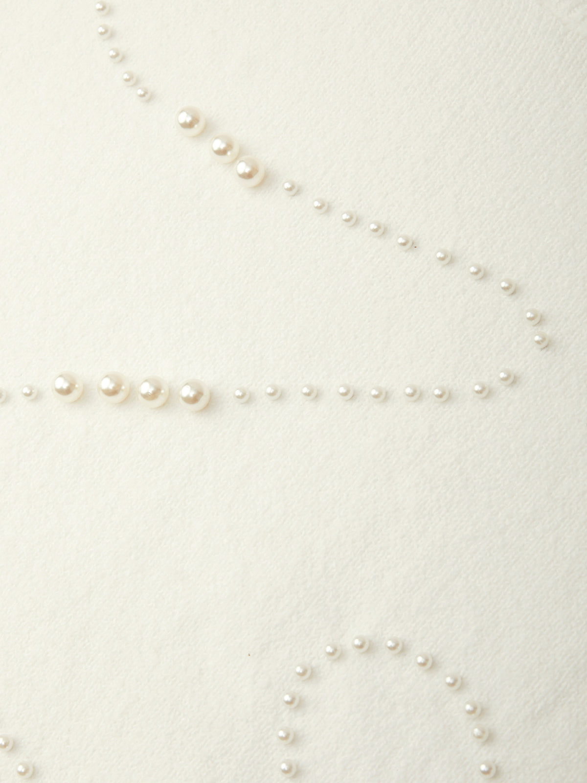 A close-up of a delicate strand of small white faux pearls laid out on a warm off-white textured fabric background.
