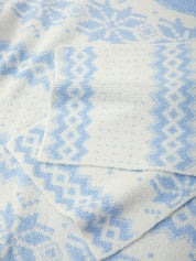 A close-up of a soft knit fabric with a light blue and white geometric Fair Isle pattern, showing the texture of the knit material.