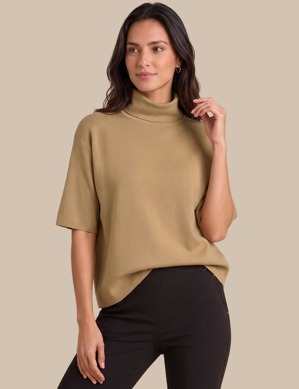 A woman modeling a short-sleeve, mock-neck knit top in camel beige, paired with black pants, against a solid beige background.