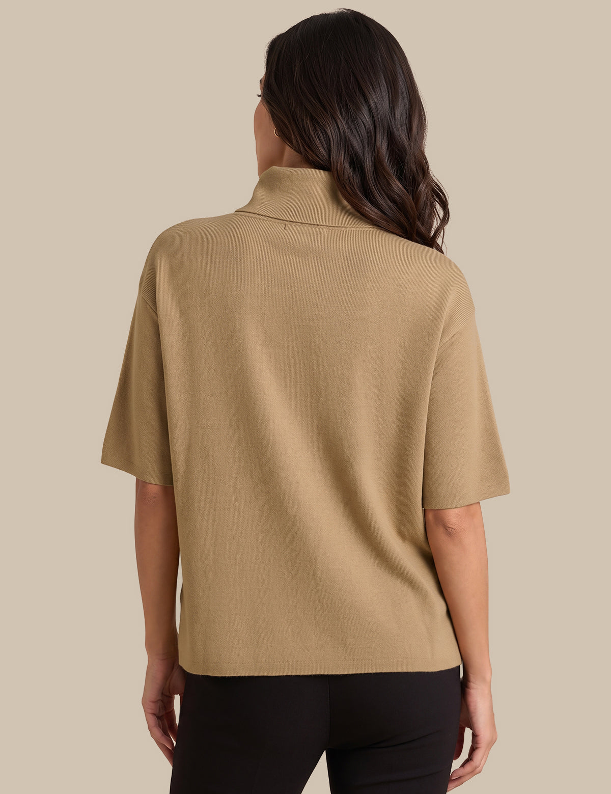 A woman shown from the back wearing a tan short-sleeve knit top and black pants against a solid beige background.