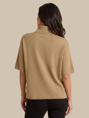 A woman shown from the back wearing a tan short-sleeve knit top and black pants against a solid beige background.