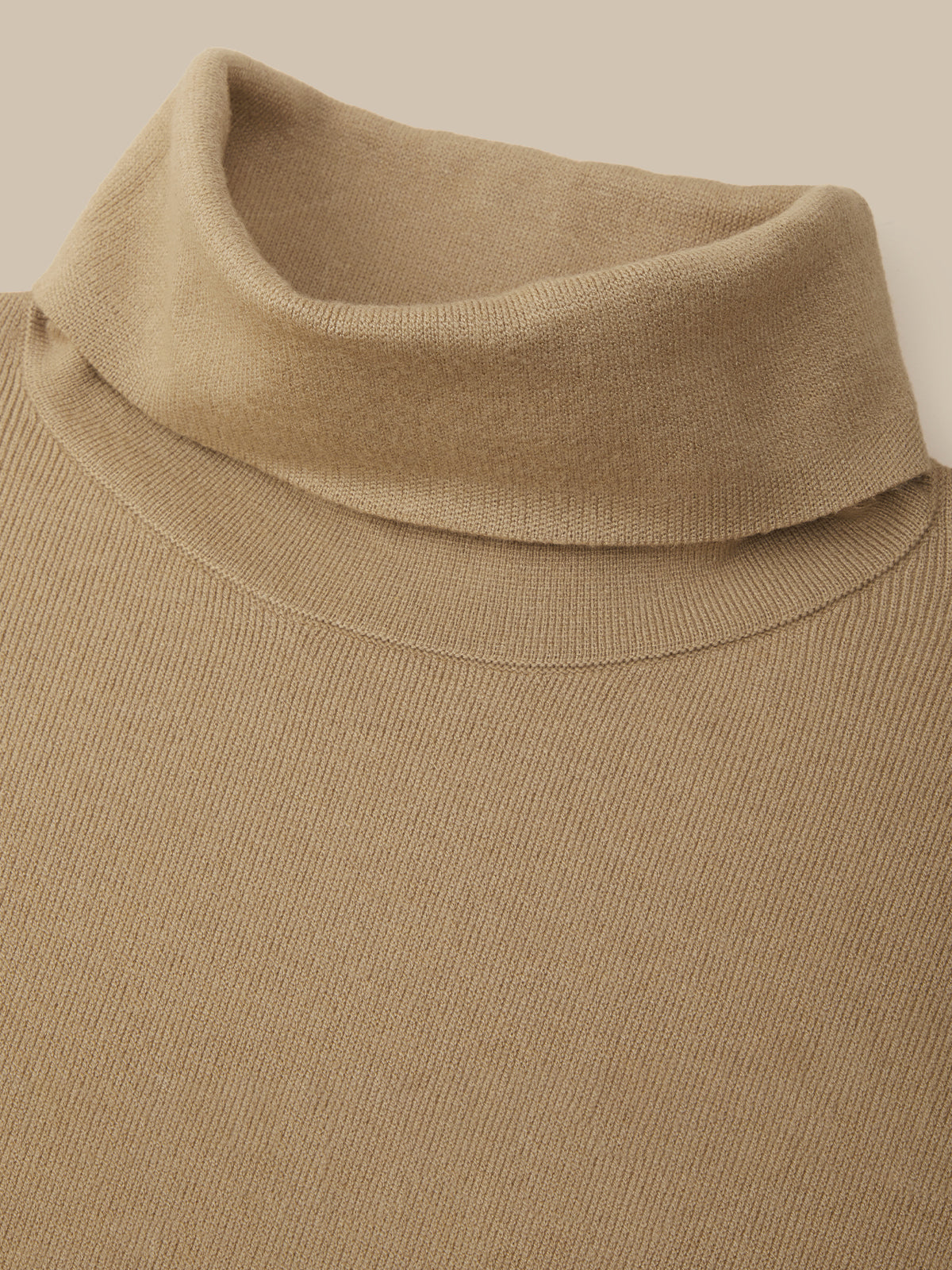 Close-up of a beige ribbed knit turtleneck sweater showing the collar and upper chest against a matching light beige background.