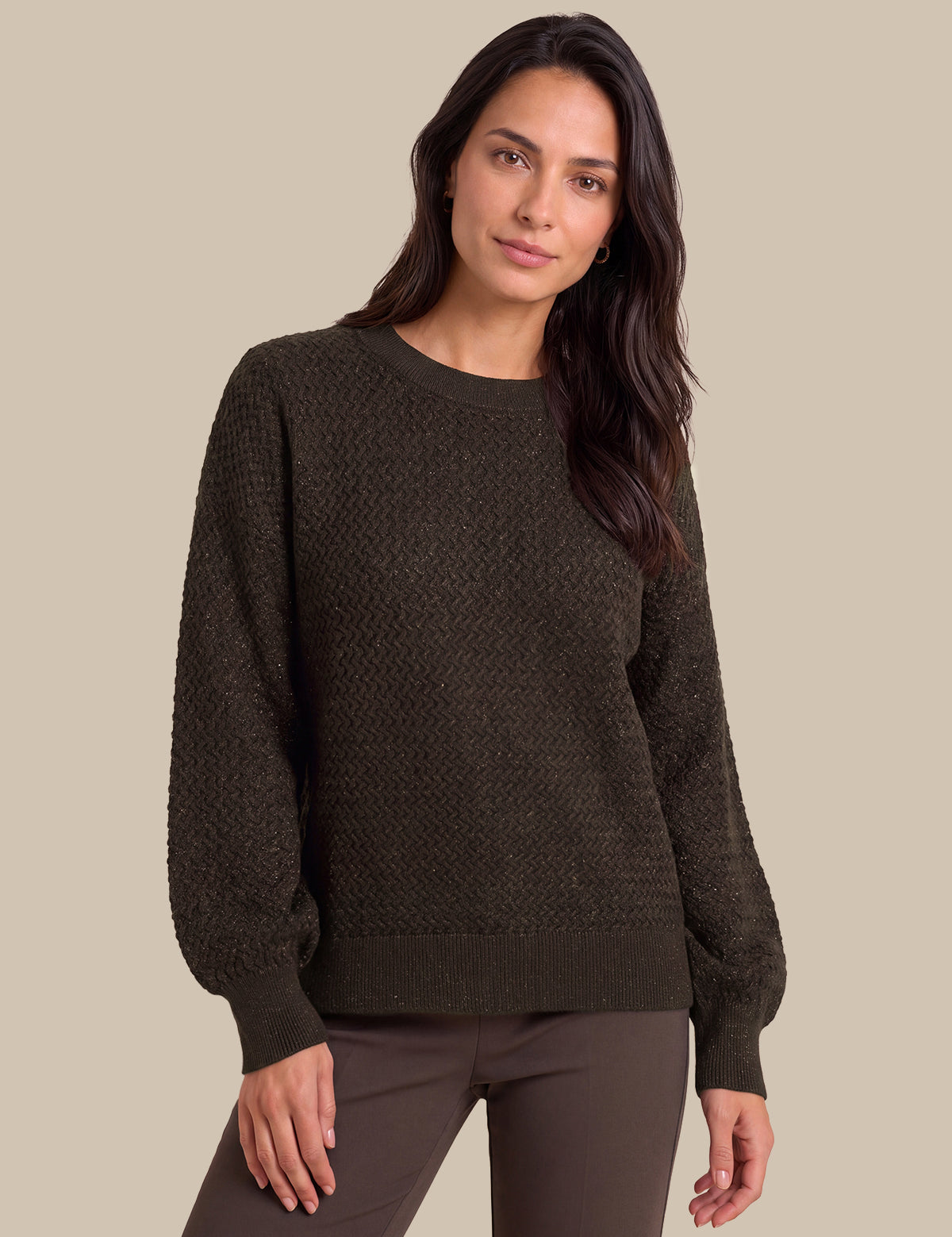 A woman modeling a dark brown textured knit sweater with balloon sleeves, paired with dark brown pants, against a solid beige background.