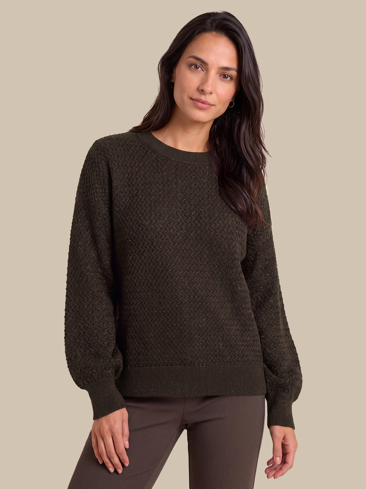 A woman modeling a dark brown textured knit sweater with balloon sleeves, paired with dark brown pants, against a solid beige background.
