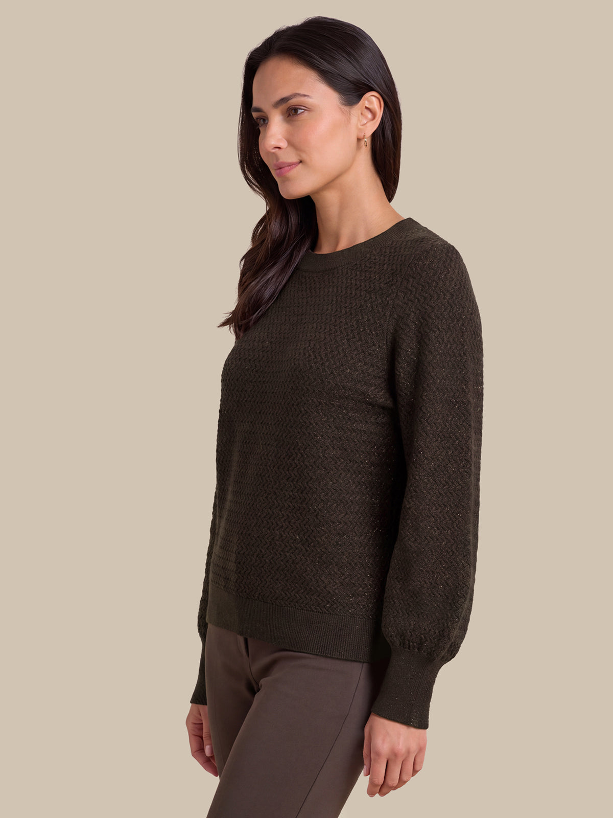 A woman wearing a dark brown textured knit sweater with long balloon sleeves, shown in a side profile against a solid beige background.